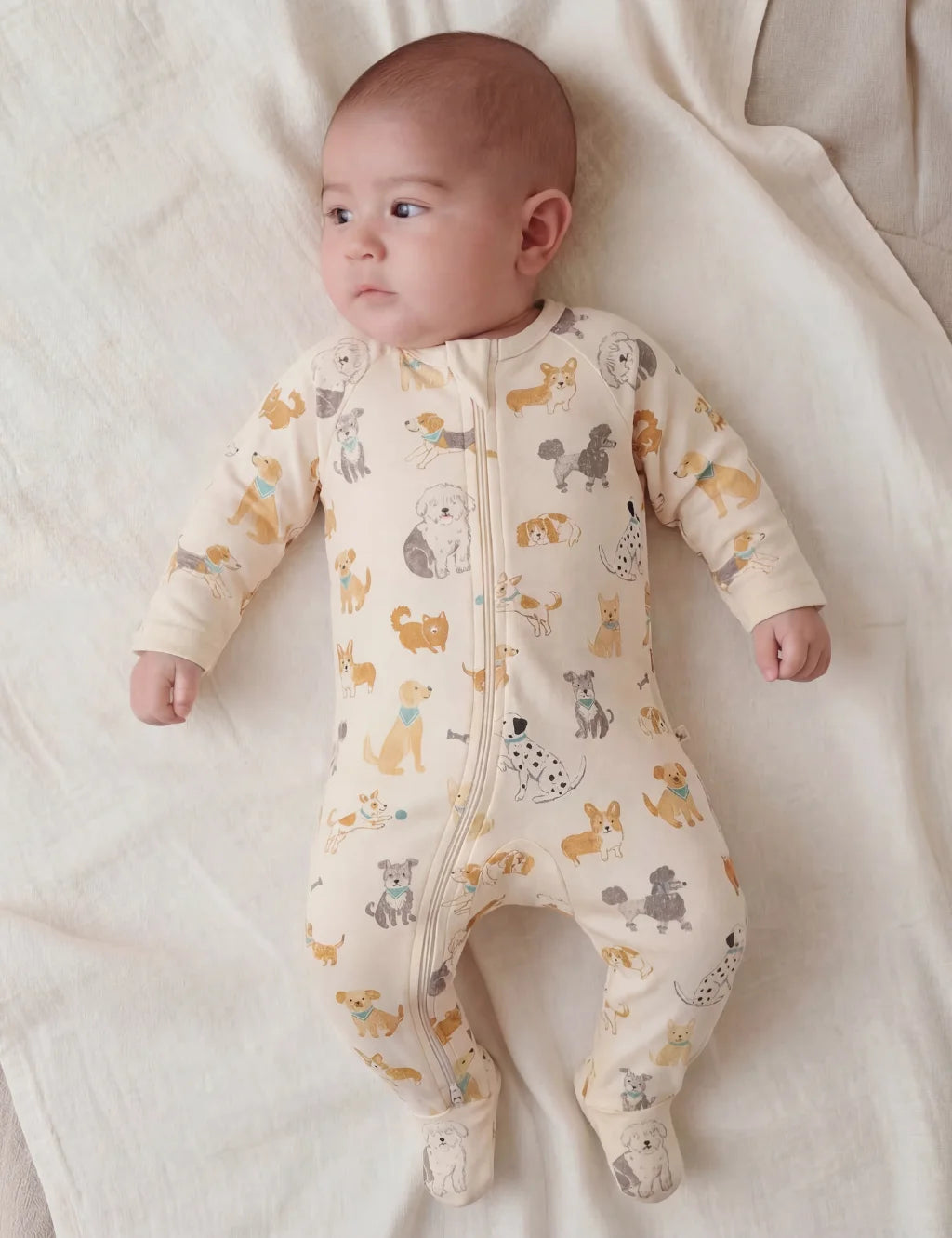 Baby wearing a cream-colored onesie with animal patterns on a white blanket