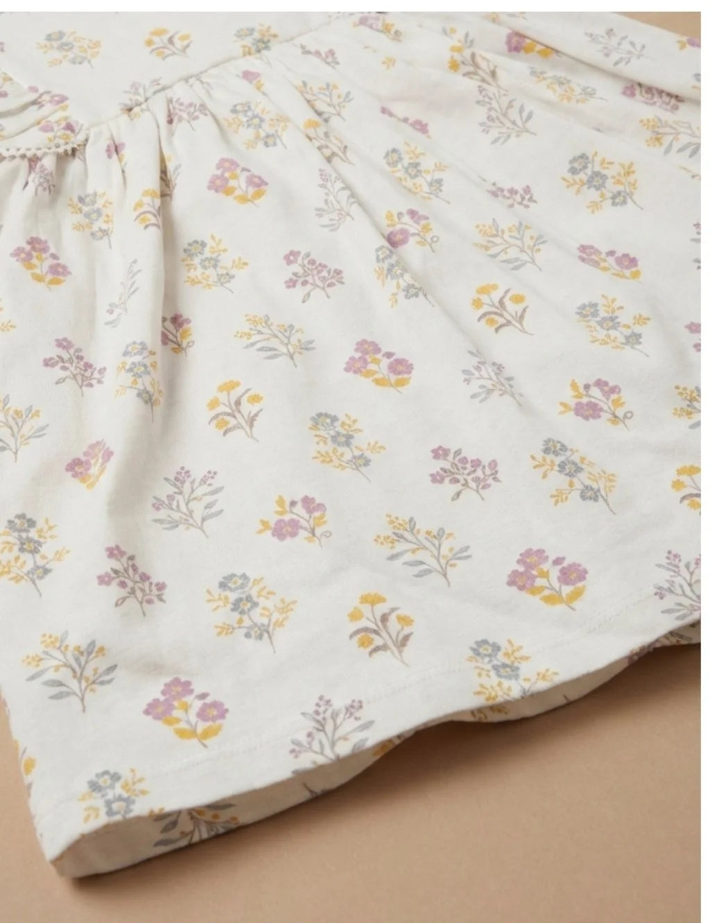 Close-up view of cream floral print cotton fabric and pleated skirt detail on a toddler dress.