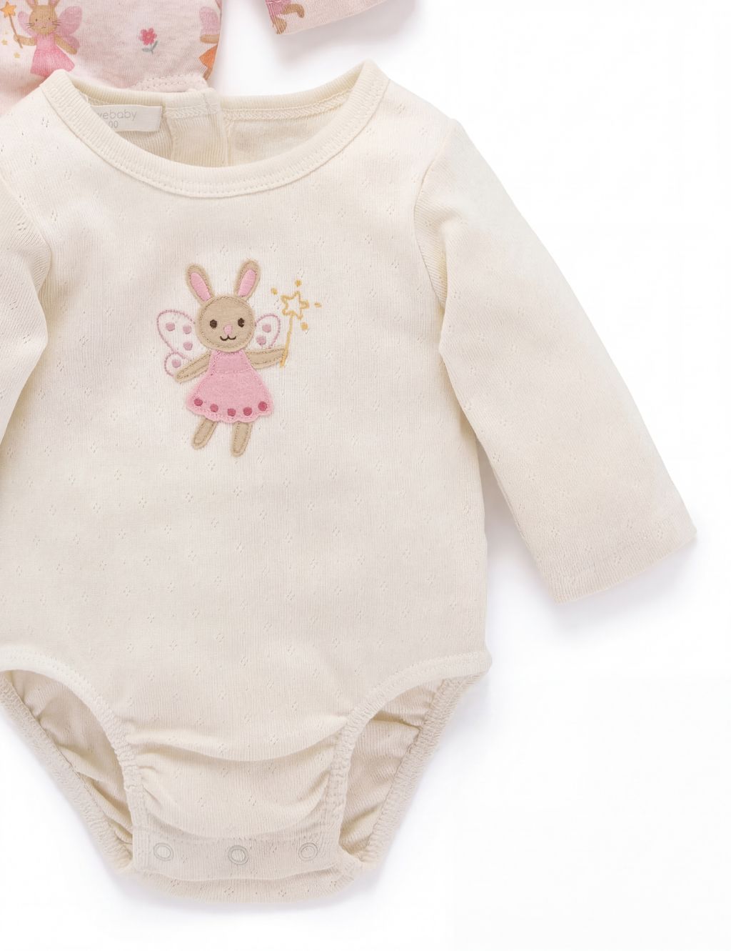 Close-up of a cream long-sleeve baby bodysuit highlighting the detailed embroidery of a fairy bunny holding a star wand on the chest.