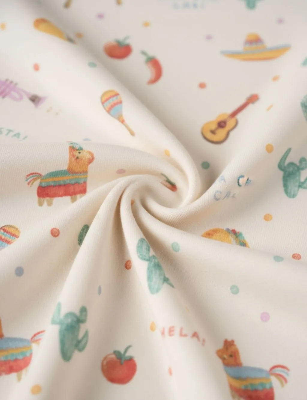 Close-up of swirled organic cotton fabric showing a fiesta print with piñatas, guitars, cacti, and sombreros