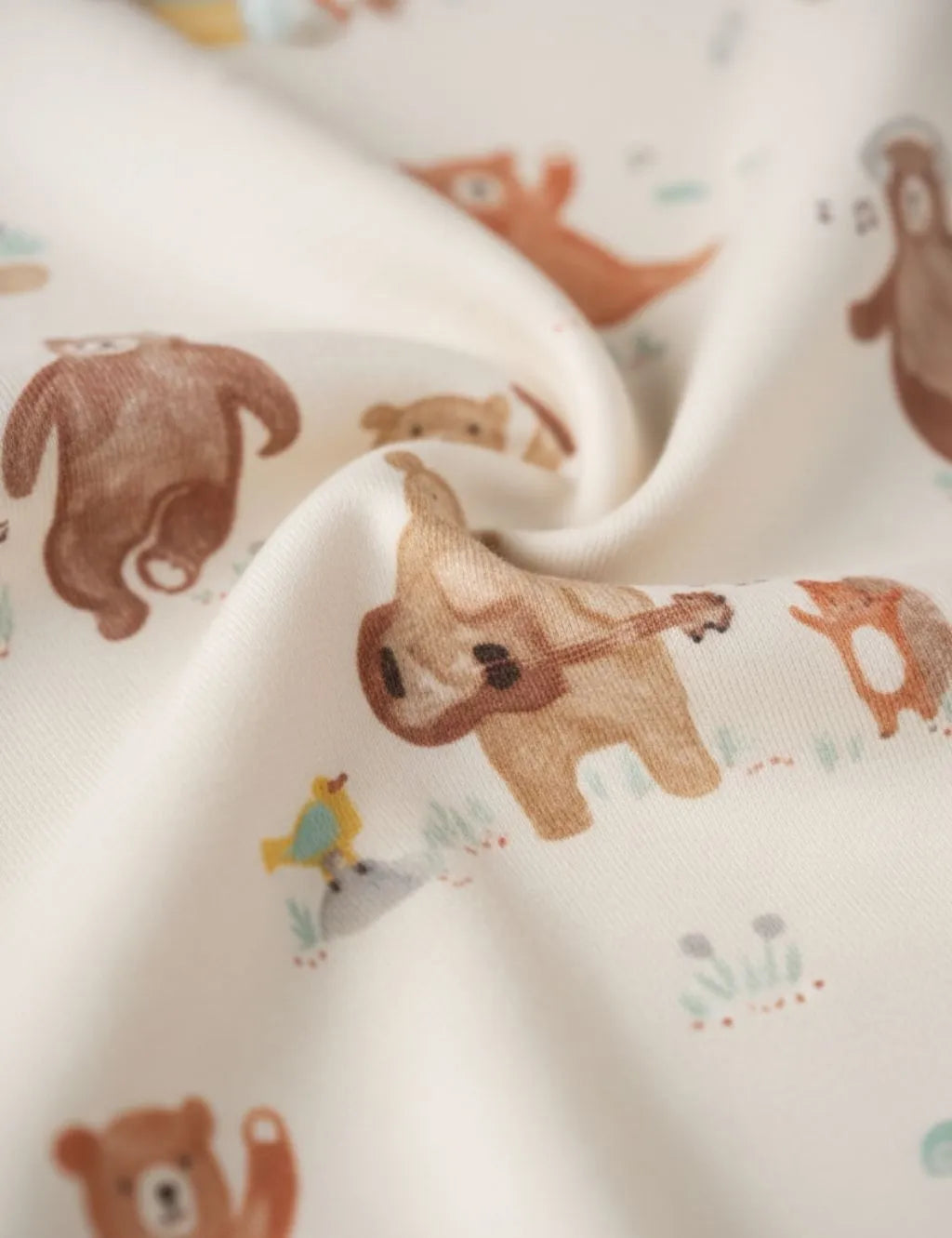 Close-up fabric detail of an organic cotton footie romper showing the soft swirled texture and musical bear print.