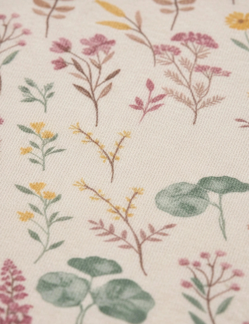 Detailed fabric close-up showcasing a cream-colored material with a delicate wildflower and botanical print featuring muted pink flowers, yellow sprigs, and green leaves.