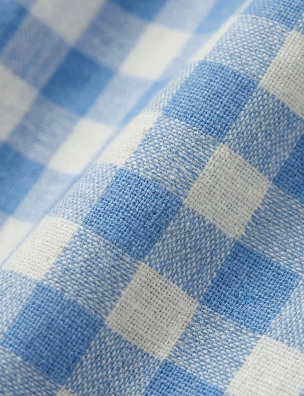 Macro fabric texture detail showing soft weave of organic cotton blue and white gingham check pattern.