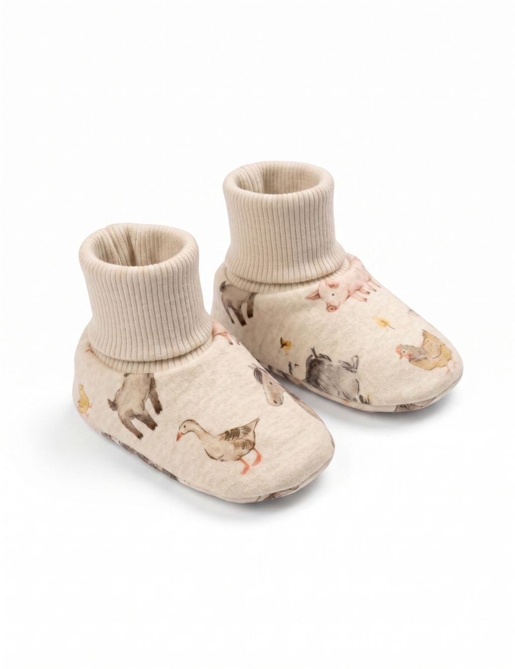 A pair of soft cream-colored baby booties featuring a charming watercolor farm animal print with a goose, a goat, and a pig, displayed against a plain white background.