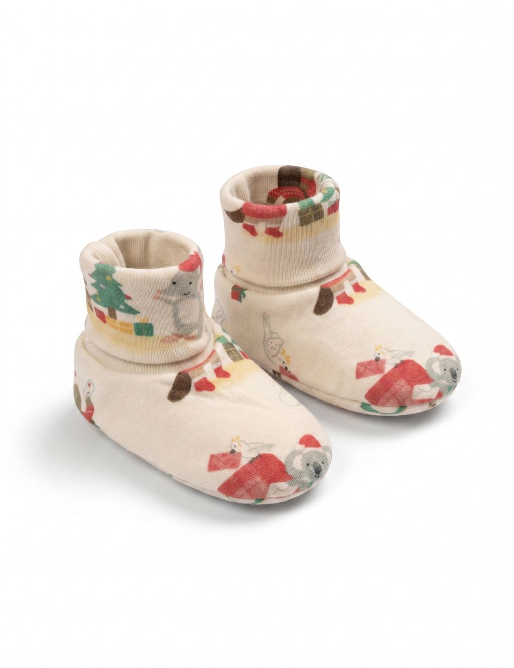 A pair of soft cream-colored baby booties featuring a festive holiday print with a koala wearing a Santa hat, presents, and a Christmas tree, displayed against a plain white background.