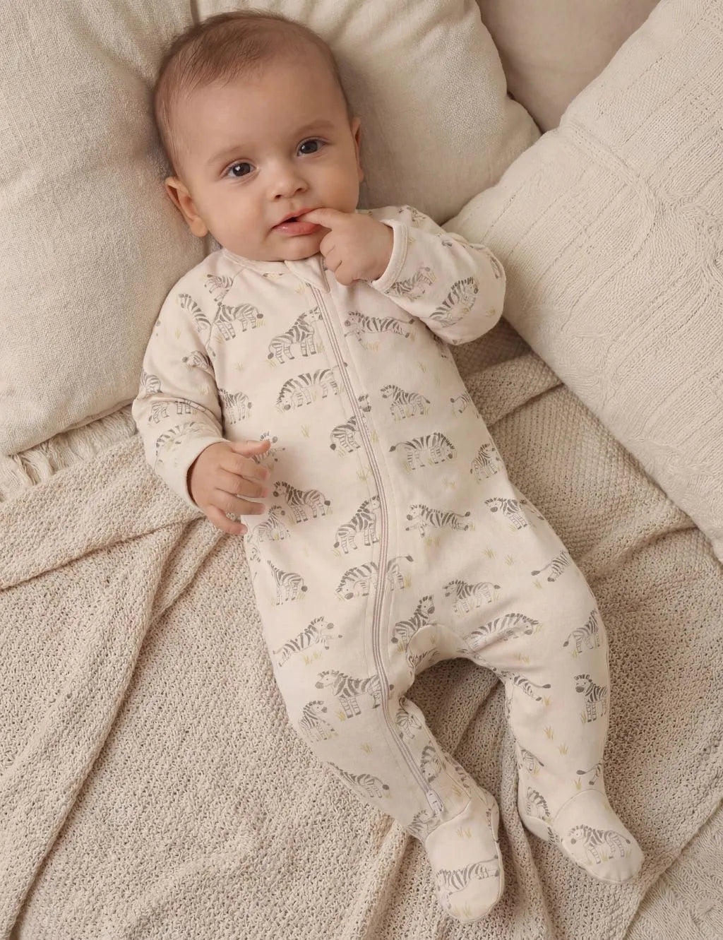 Newborn baby wearing a cream organic cotton zipper romper featuring a grazing zebra print.