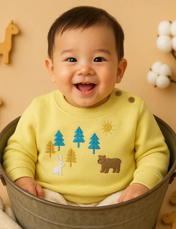 Happy baby wearing a soft yellow long-sleeve sweatshirt with cute embroidered forest animals (bear, rabbit) and trees. Shop adorable baby clothes online in India.