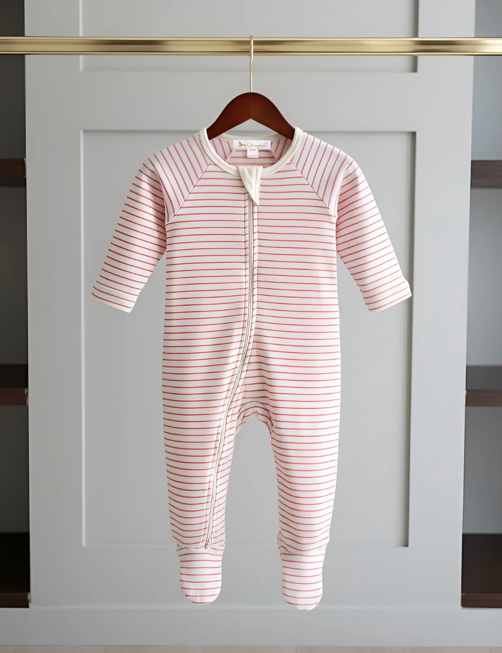 Pink and white striped baby onesie on a hanger against a gray wall.