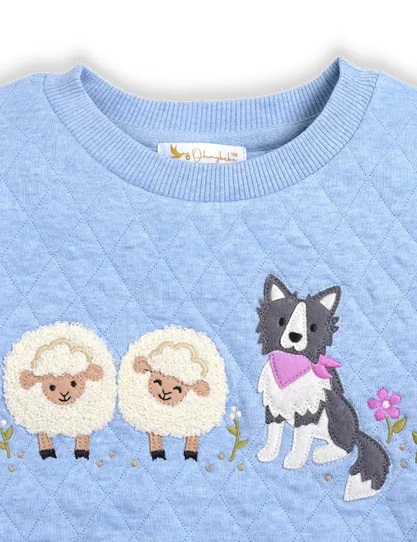 Light blue quilted fabric with embroidered two fluffy sheep and a black and white dog wearing a pink scarf