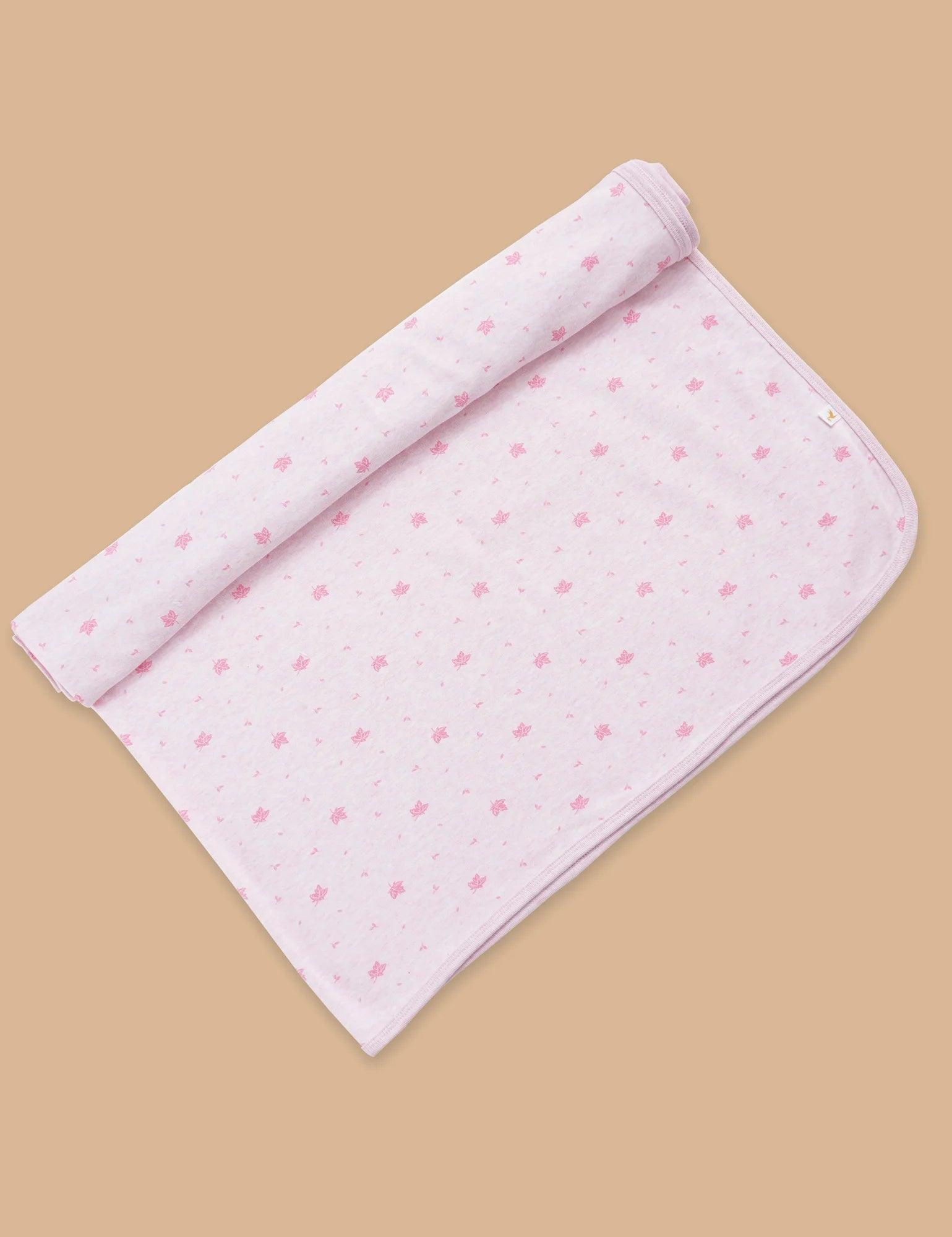 Rolled soft pink muslin baby swaddle with small maple leaf print on beige background