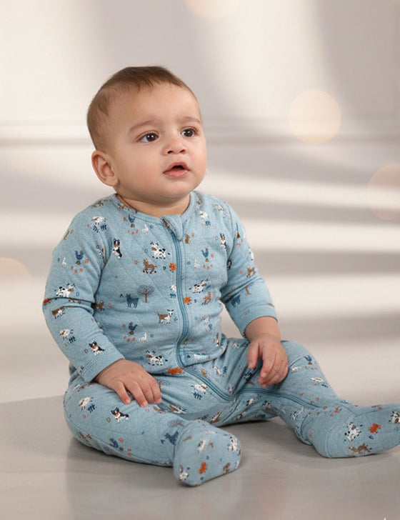 Baby in blue winter romper with animal prints sitting on floor in soft lighting