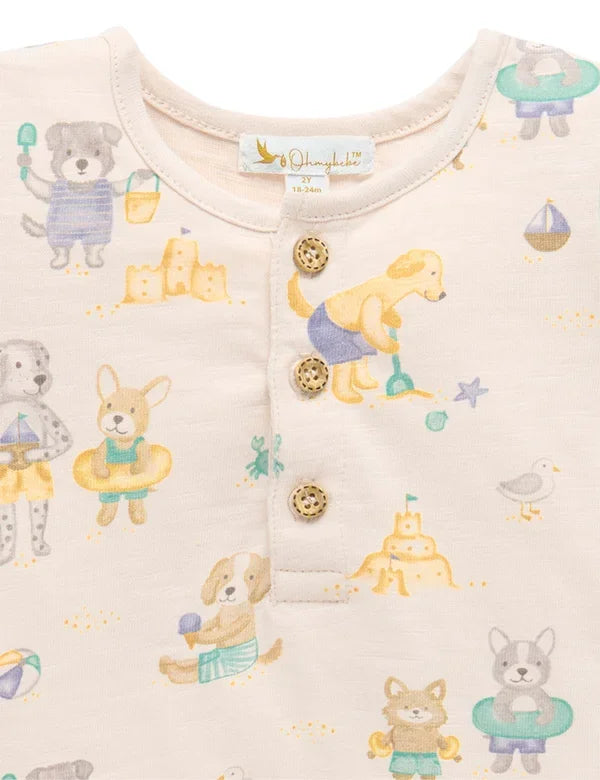 Close-up of cream baby romper with beach dogs print, wooden button neckline detail, organic fabric