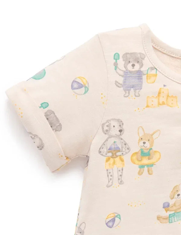 Close-up of baby romper sleeve and fabric with playful dog beach print including sandcastle, beach ball, and dogs in swimwear