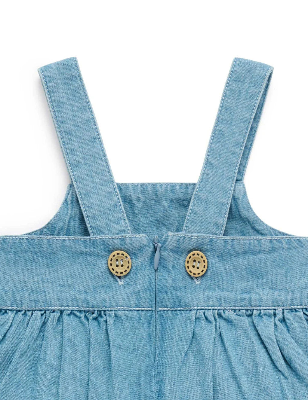 Close-up of a blue denim dress with straps and buttons on a white background