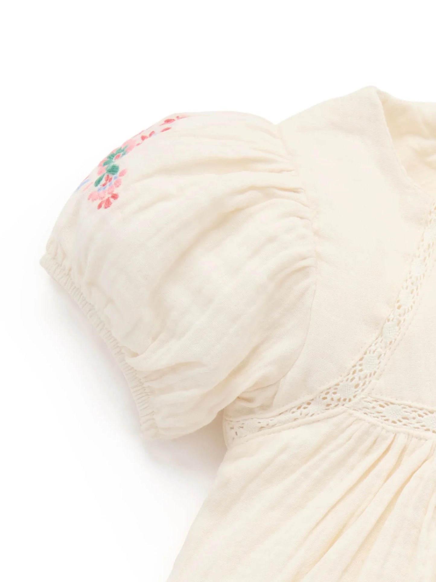 Close-up of a cream-colored garment with floral embroidery on a white background