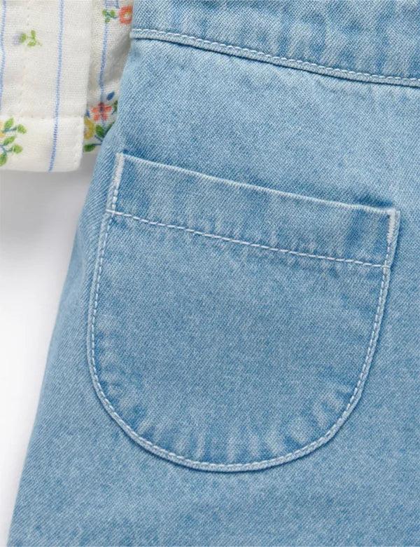 Light blue denim baby shorts featuring a close-up of a stitched back pocket with part of a floral patterned garment visible