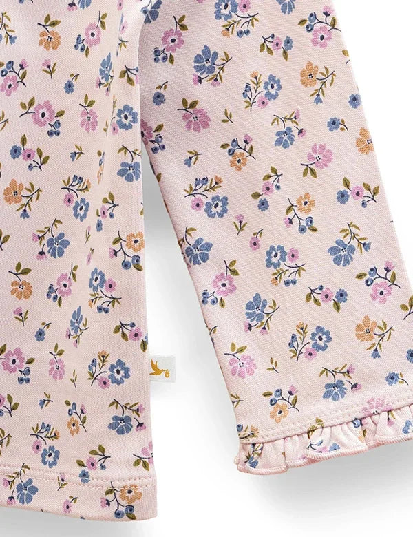 Close-up of baby top sleeve with pink fabric and small blue, orange, and purple floral print with ruffle detail