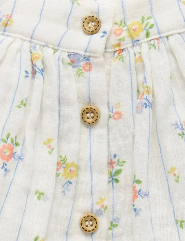 Close-up of white organic cotton fabric with blue stripes, floral print, and wooden buttons on a top bodice