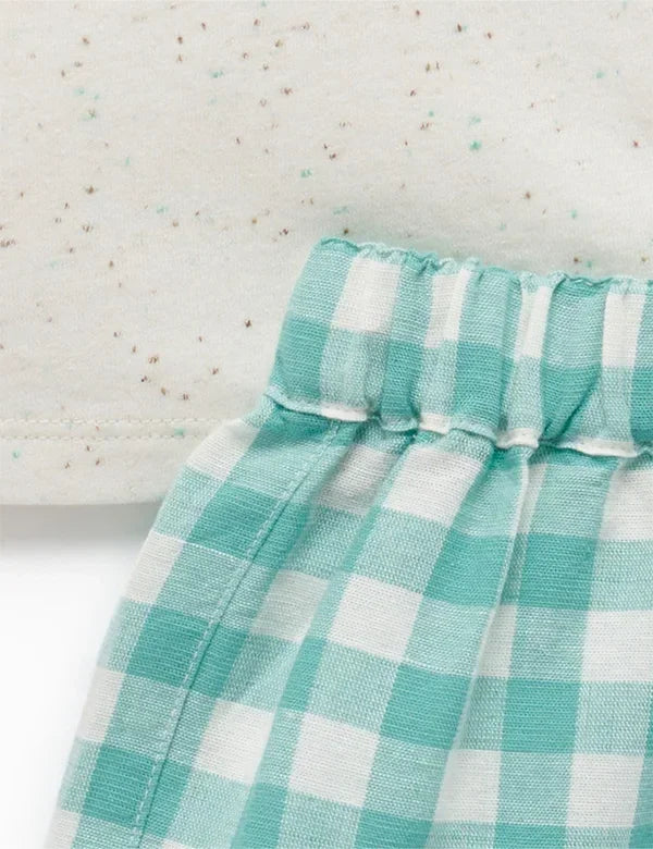 Close-up of baby outfit fabric showing mint green gingham shorts and cream speckled knit top detail