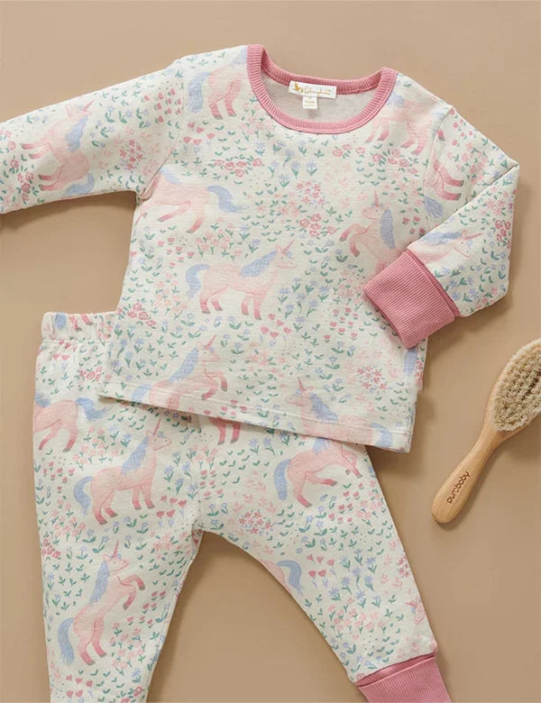 Pink and blue unicorn print organic baby pajama set with ribbed pink cuffs and neckline, flatlay with baby hairbrush