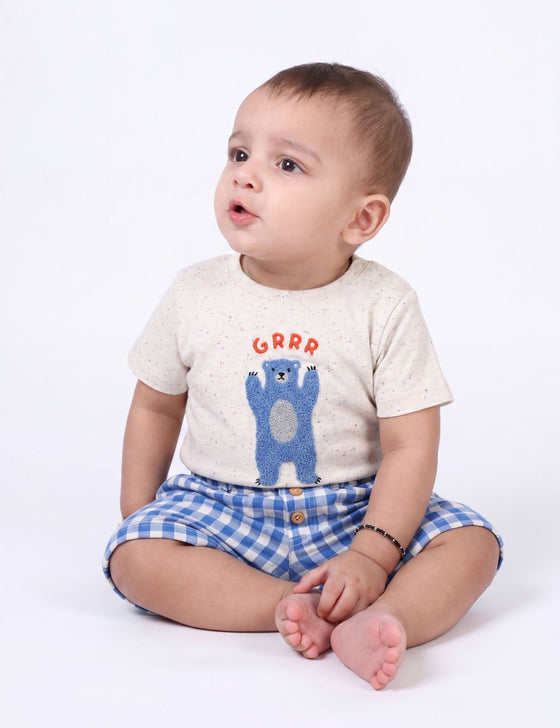 Baby sitting down wearing an organic cotton off-white t-shirt with a blue bear print and blue gingham shorts