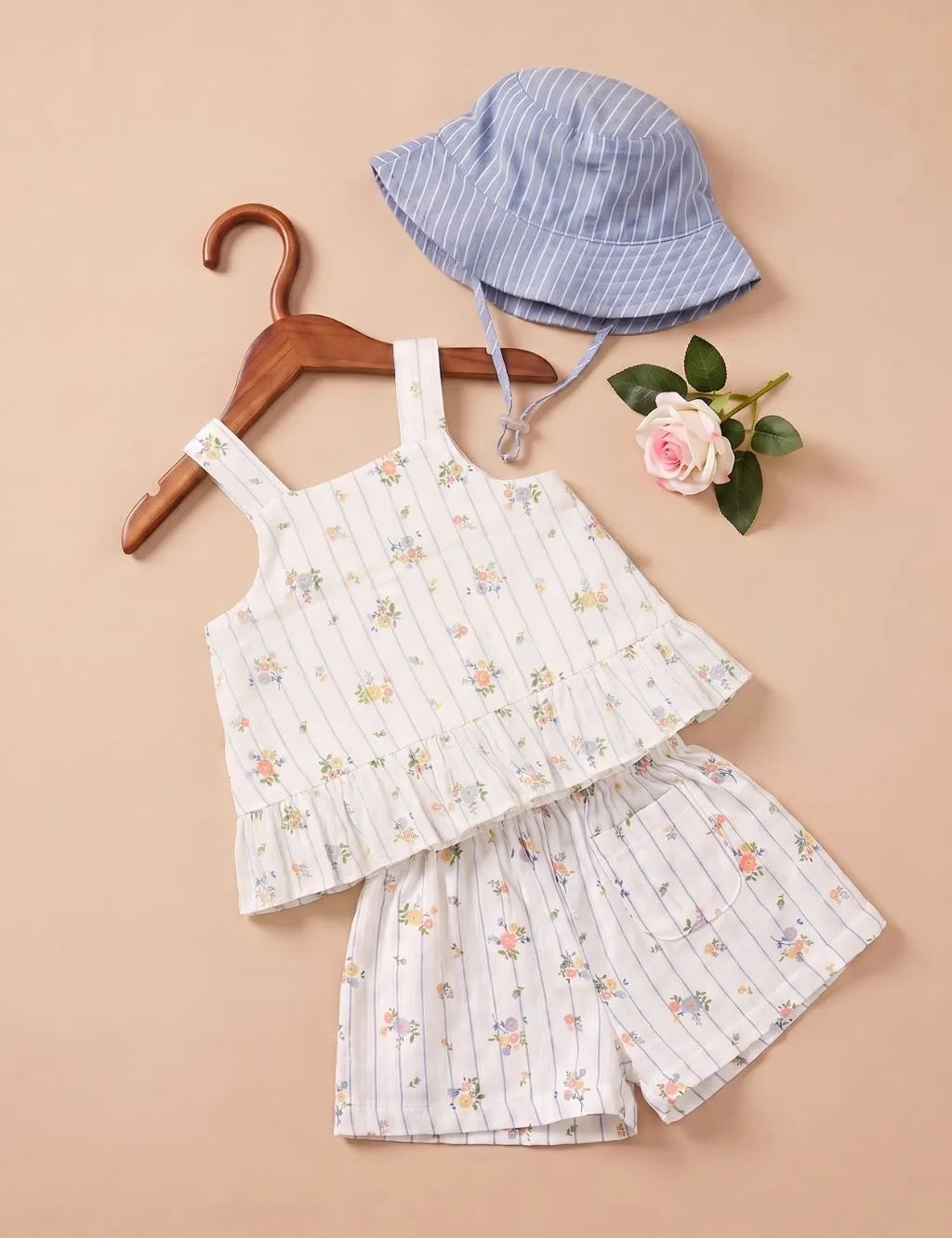 Flatlay of an organic cotton blue striped floral peplum top and matching shorts set, paired with a bucket hat.