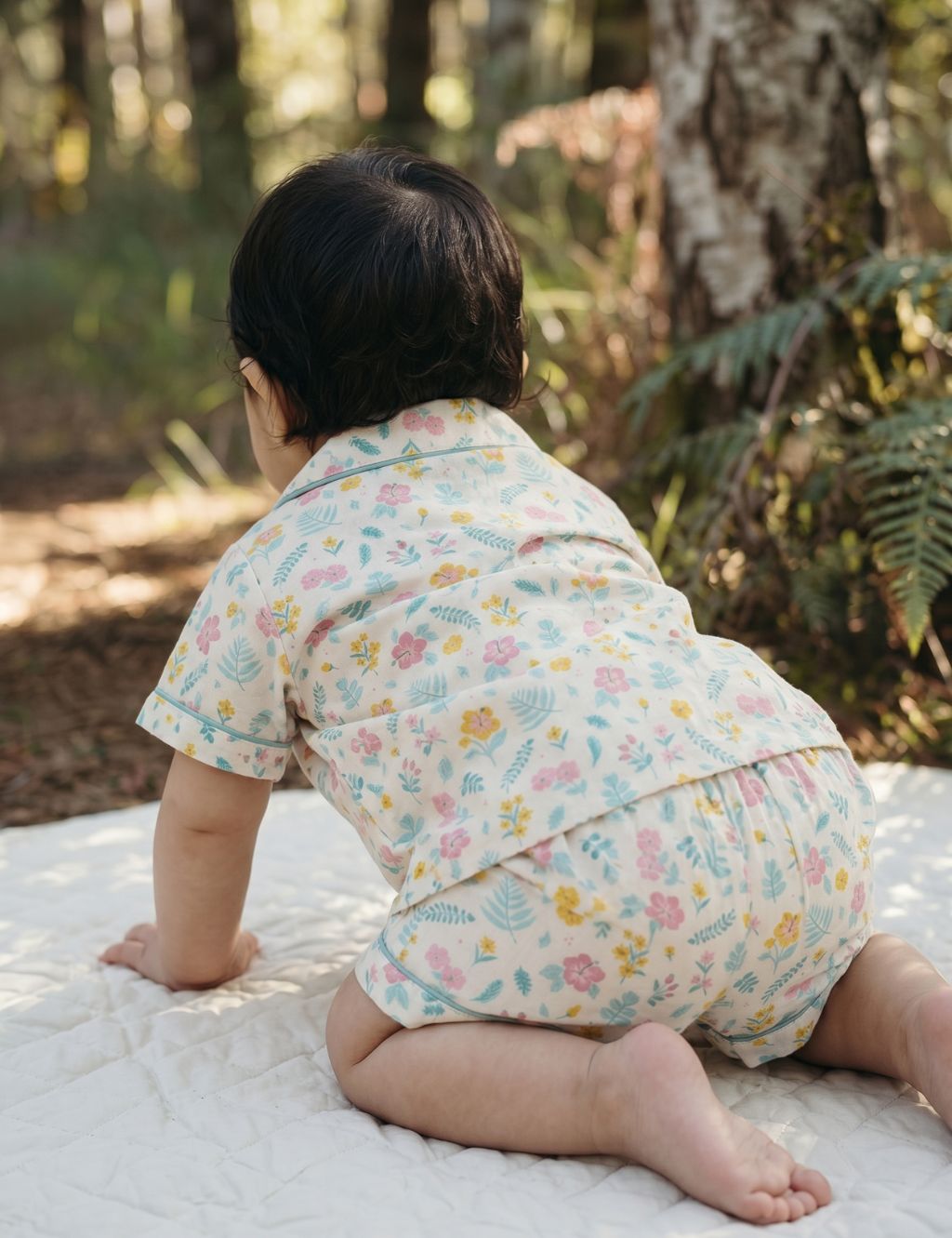 Back view of a baby crawling on an outdoor blanket and wearing an organic cotton botanical floral print shirt and shorts set.