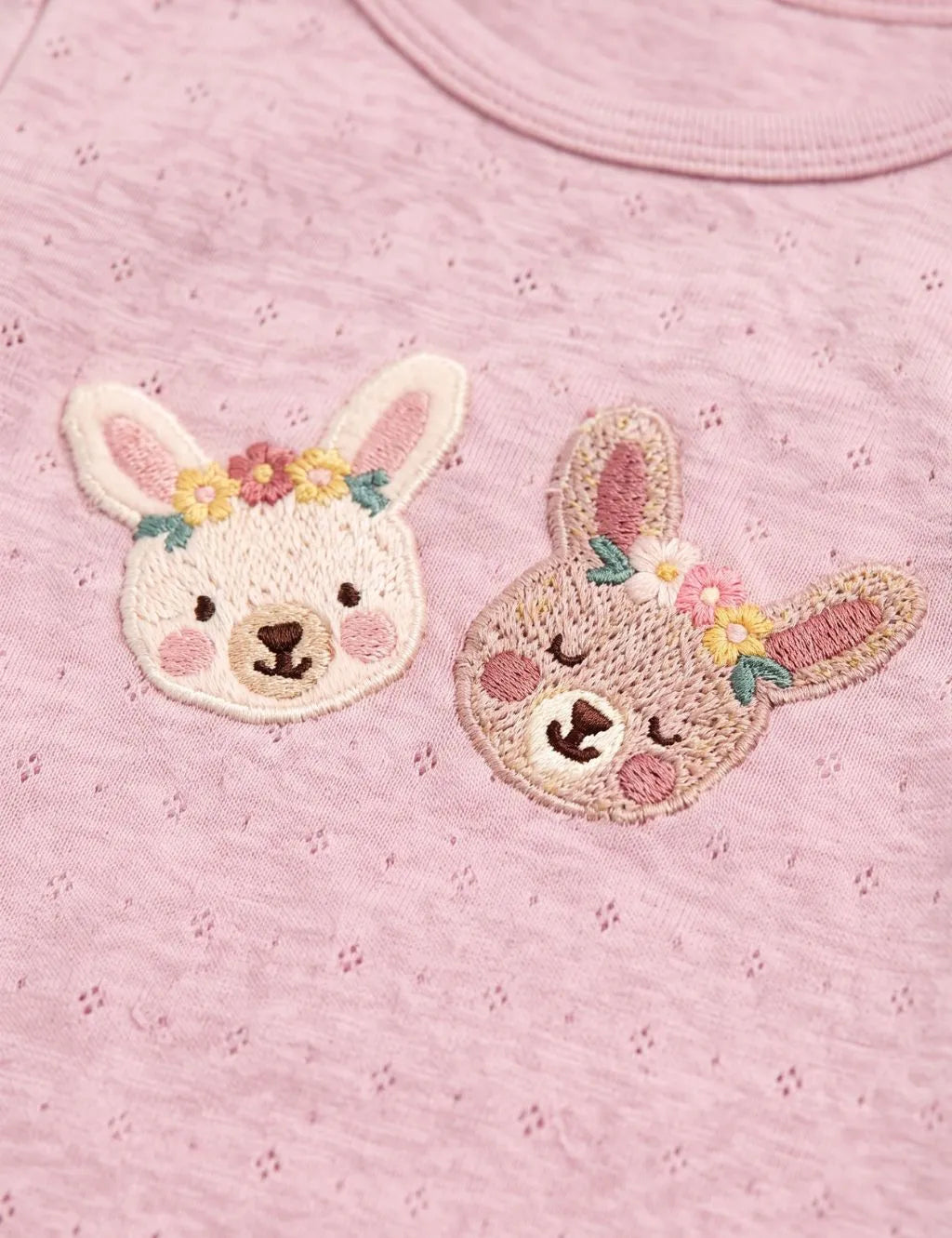 Close-up of the delicate embroidery featuring two cute bunnies with floral crowns on an organic cotton pink onesie.