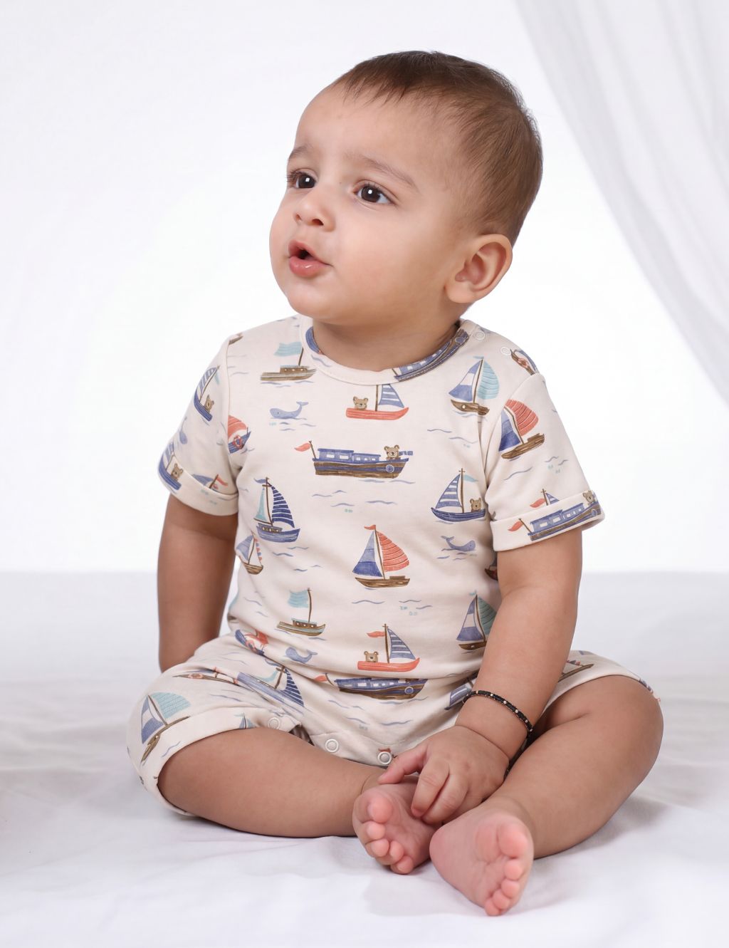 Baby sitting on a white surface wearing a cream organic cotton short-sleeve baby romper featuring a nautical cloud yacht and sailboat print.