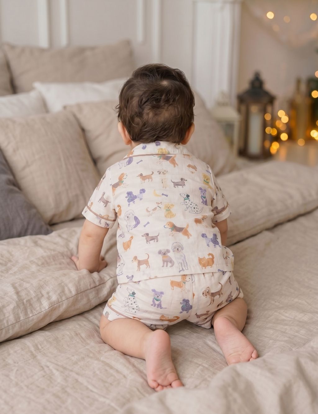 Back view of a baby crawling on a bed and wearing an organic cotton short-sleeve shirt and shorts set with a playful dog print.