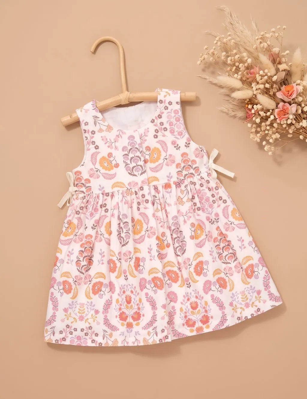Organic cotton sleeveless floral print dress hanging on a wooden hanger with dried flowers beside it