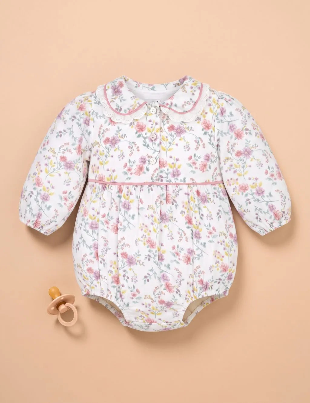 Flatlay of an organic cotton floral print long-sleeve onesie with a pink scalloped collar and pacifier.