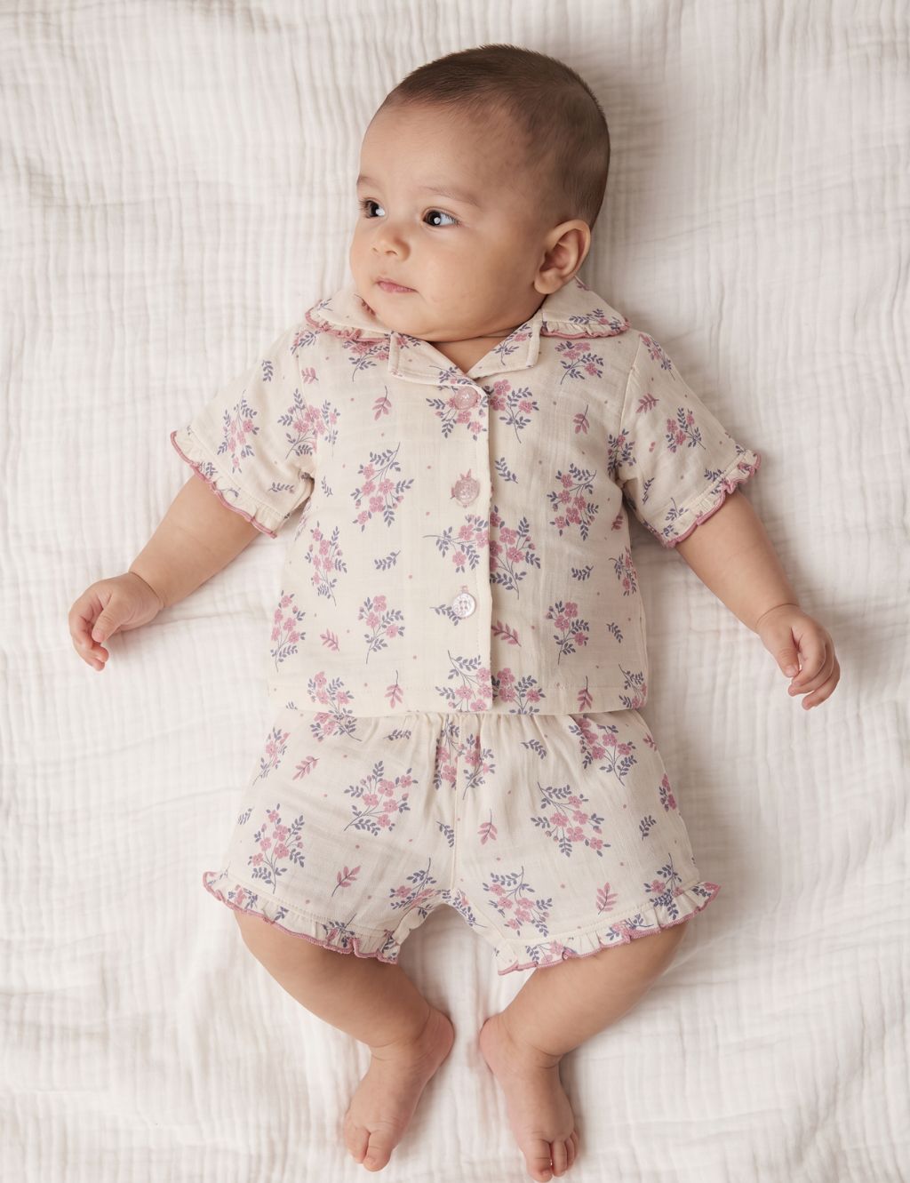 Baby lying down and wearing an organic cotton short-sleeve shirt and matching shorts set with a pink floral print.