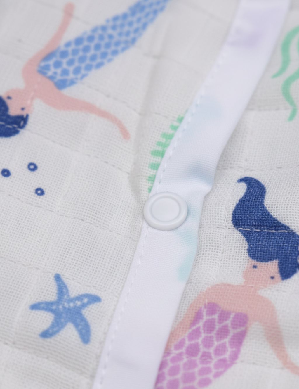 Close-up of snap buttons and fabric trim on the organic cotton onesie with a colorful mermaid print.