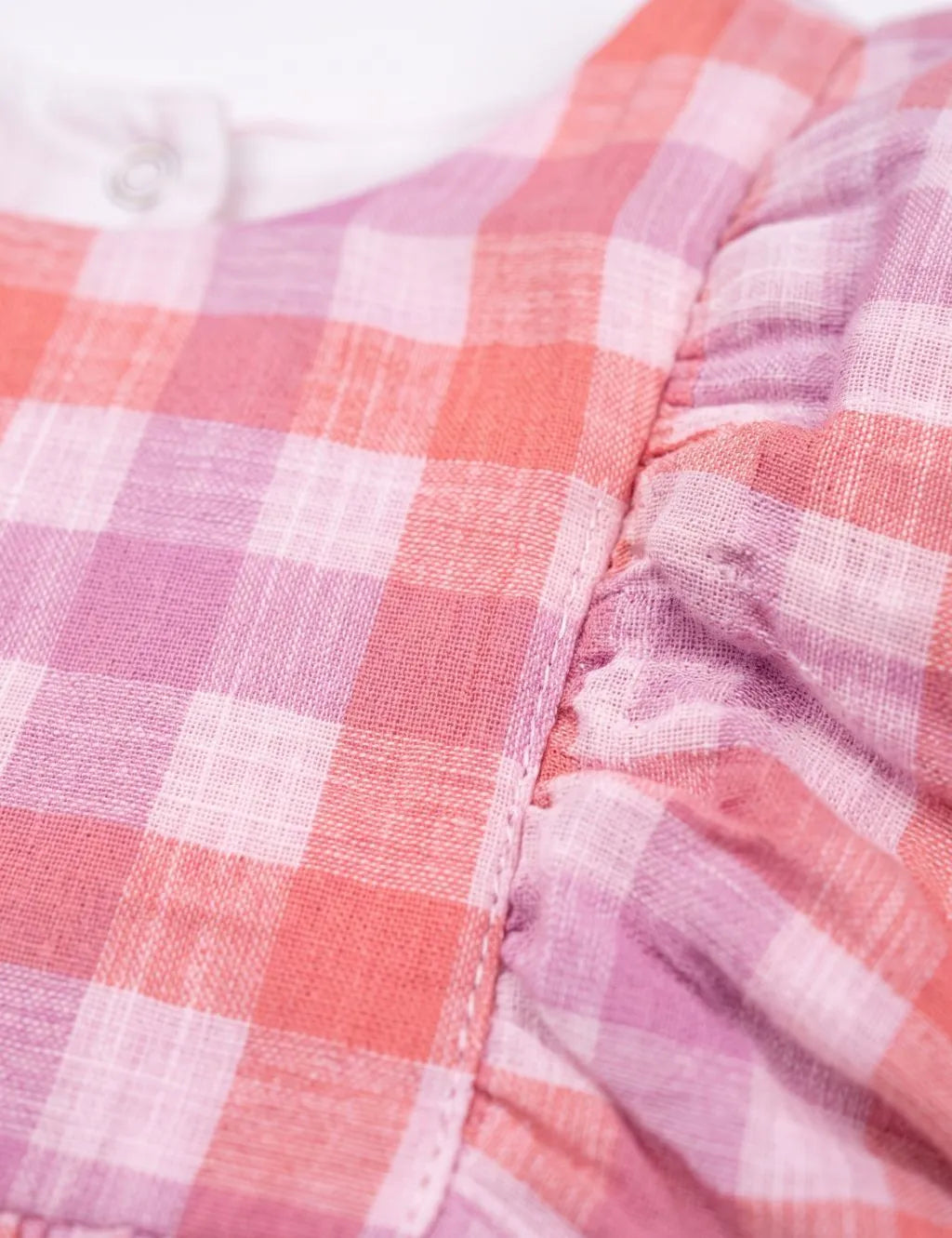 Close-up of the textured fabric, stitching, and ruffled shoulder detail on the organic cotton pink and purple checkered dress.