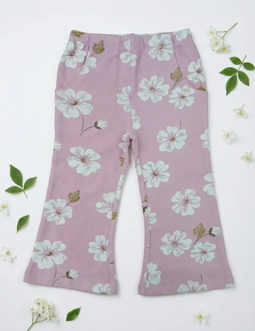 Flatlay of organic cotton pink pants featuring an all-over white floral print, pockets, and a flared cut.