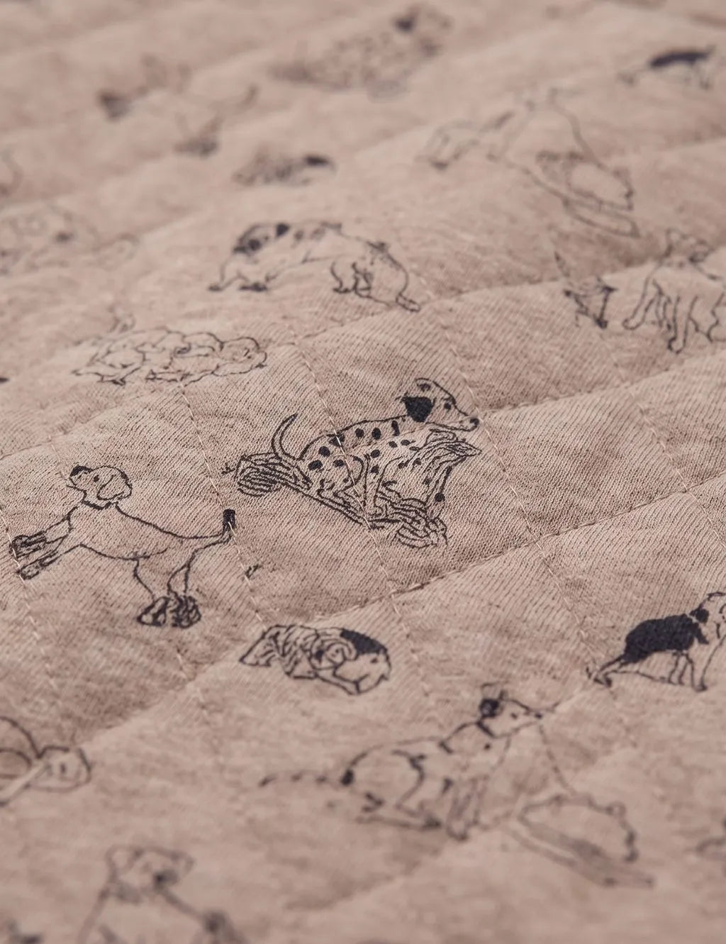 Close-up texture view of beige quilted organic cotton fabric featuring an allover dog illustration print
