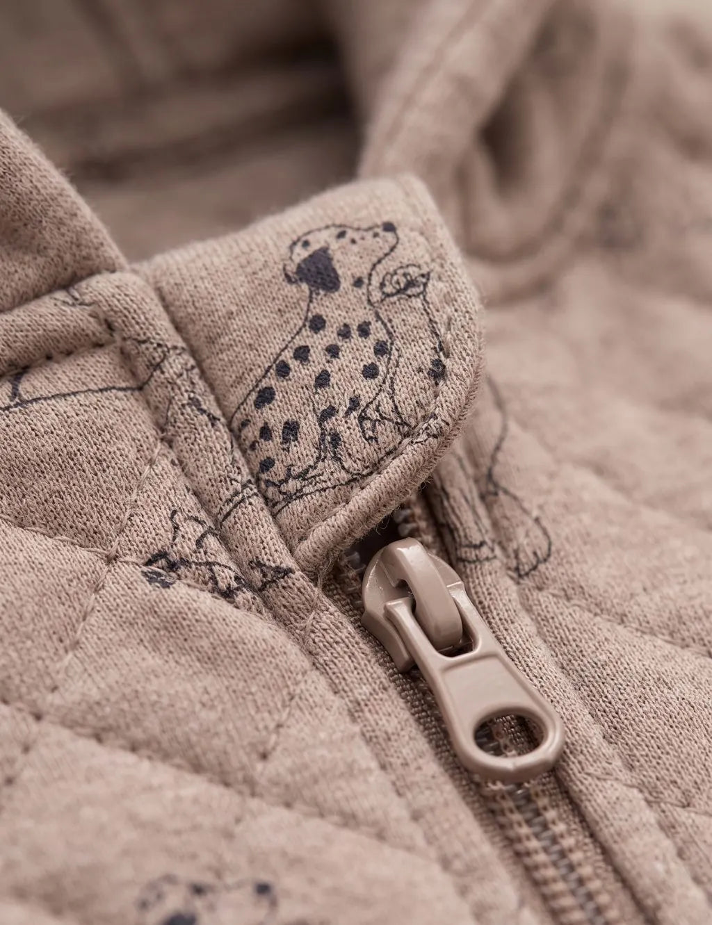 Close-up detail of zipper pull and chin guard on a quilted beige organic cotton baby romper with dog print