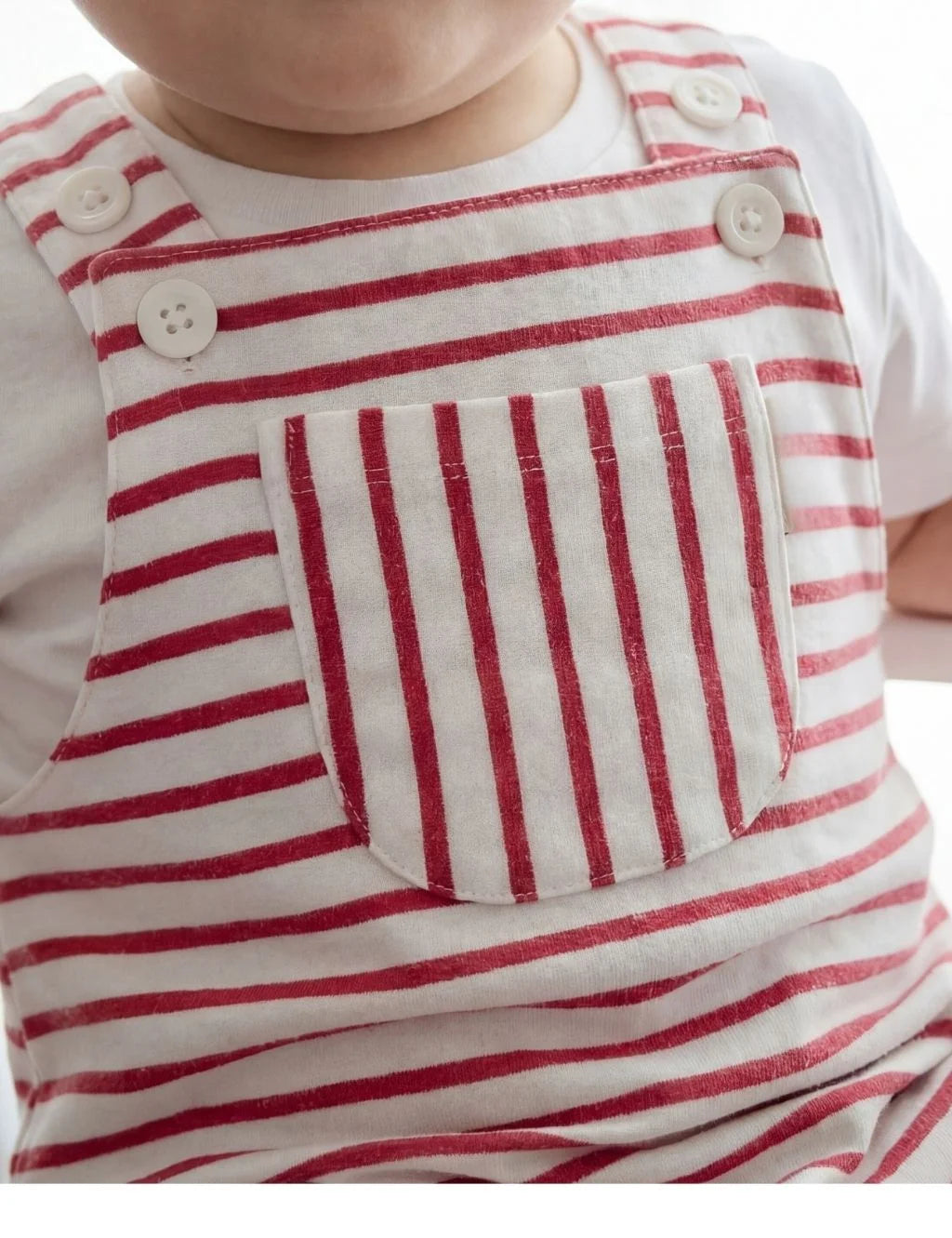 Close-up of an organic cotton red and white striped onesie detailing the front pocket and white button closures.