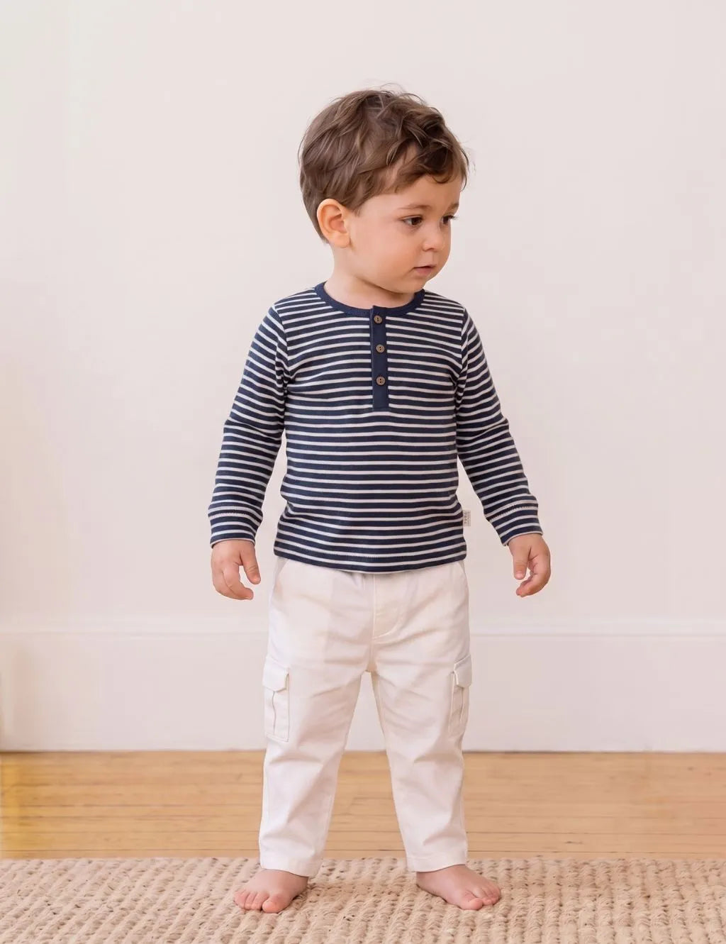 Toddler boy wearing an organic cotton navy and white striped long-sleeve polo shirt with matching white pants.