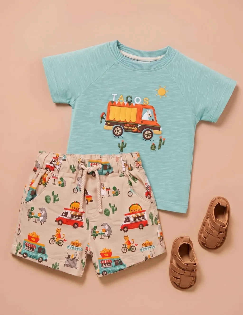 Flatlay of an organic cotton green taco food truck print top, patterned shorts with a drawstring, and brown sandals