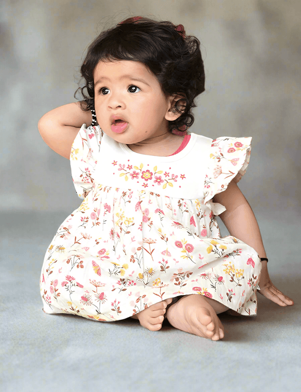 Adorable baby, who appears to be of South Asian descent, wearing a 100% organic cotton floral print dress and matching headband. Soft and sweet for your little one. Shop India.