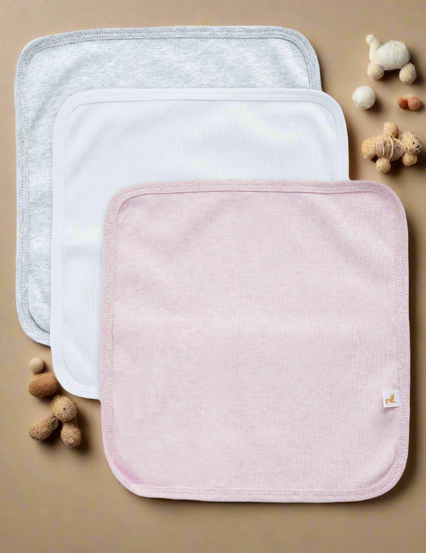 Set of three soft organic cotton burp cloths in grey marl, white, and light pink. Essential for feeding and protecting baby's clothes. Shop baby care items India.
