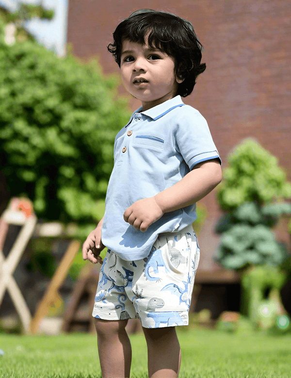 Cute toddler, who appears to be of South Asian descent, wearing a 100% organic cotton sky blue polo tee and dinosaur print shorts. Shop organic baby clothes India.