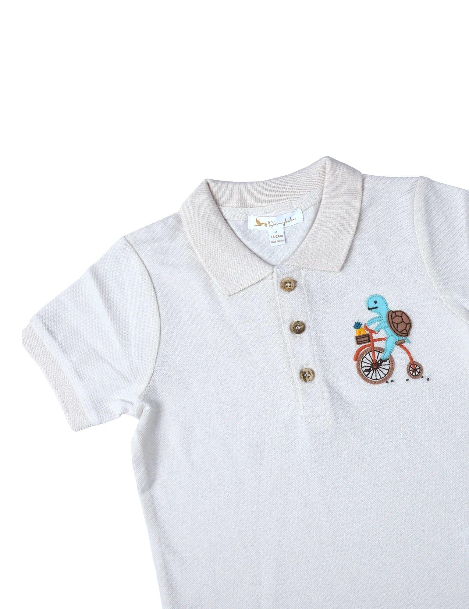 White organic cotton baby polo shirt with beige collar and turtle on bicycle applique