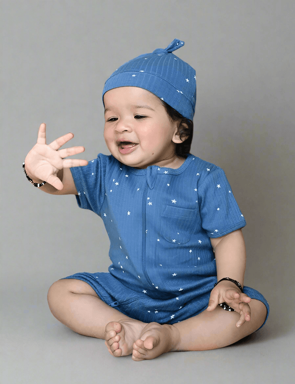  Adorable baby, who appears to be of South Asian descent, sitting and reaching out, wearing a soft blue 100% organic cotton star print romper and knot cap set. Shop comfy baby wear India.