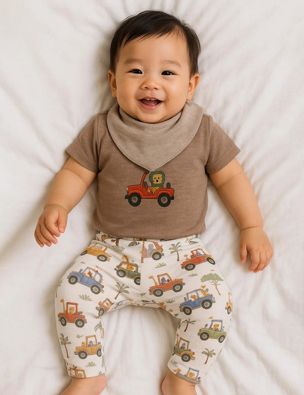 Adorable baby, who appears to be of East Asian descent, wearing a 100% organic cotton lion-themed bodysuit, leggings, and bib set. Soft and stylish for your little one. Shop India.