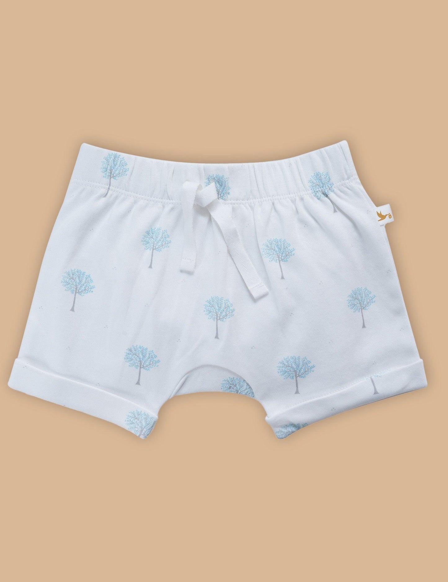 White organic cotton baby shorts with blue tree prints and drawstring on beige background