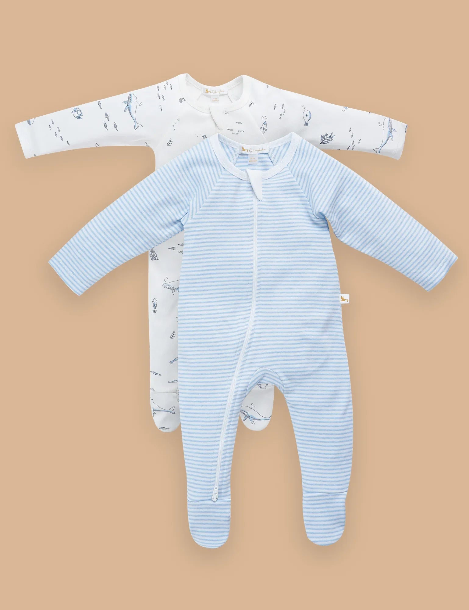 Two organic cotton baby sleepsuits flatlay, one blue striped, one white with ocean prints