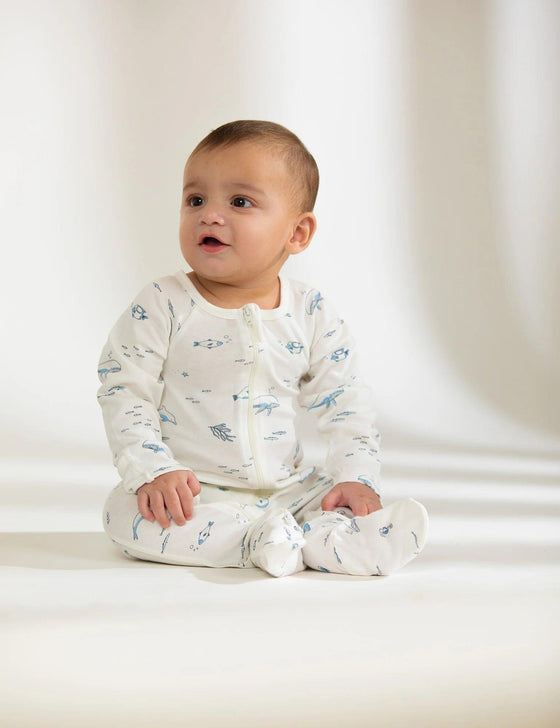 Baby sitting in organic cotton sleepsuit with blue nautical sea life print on white background